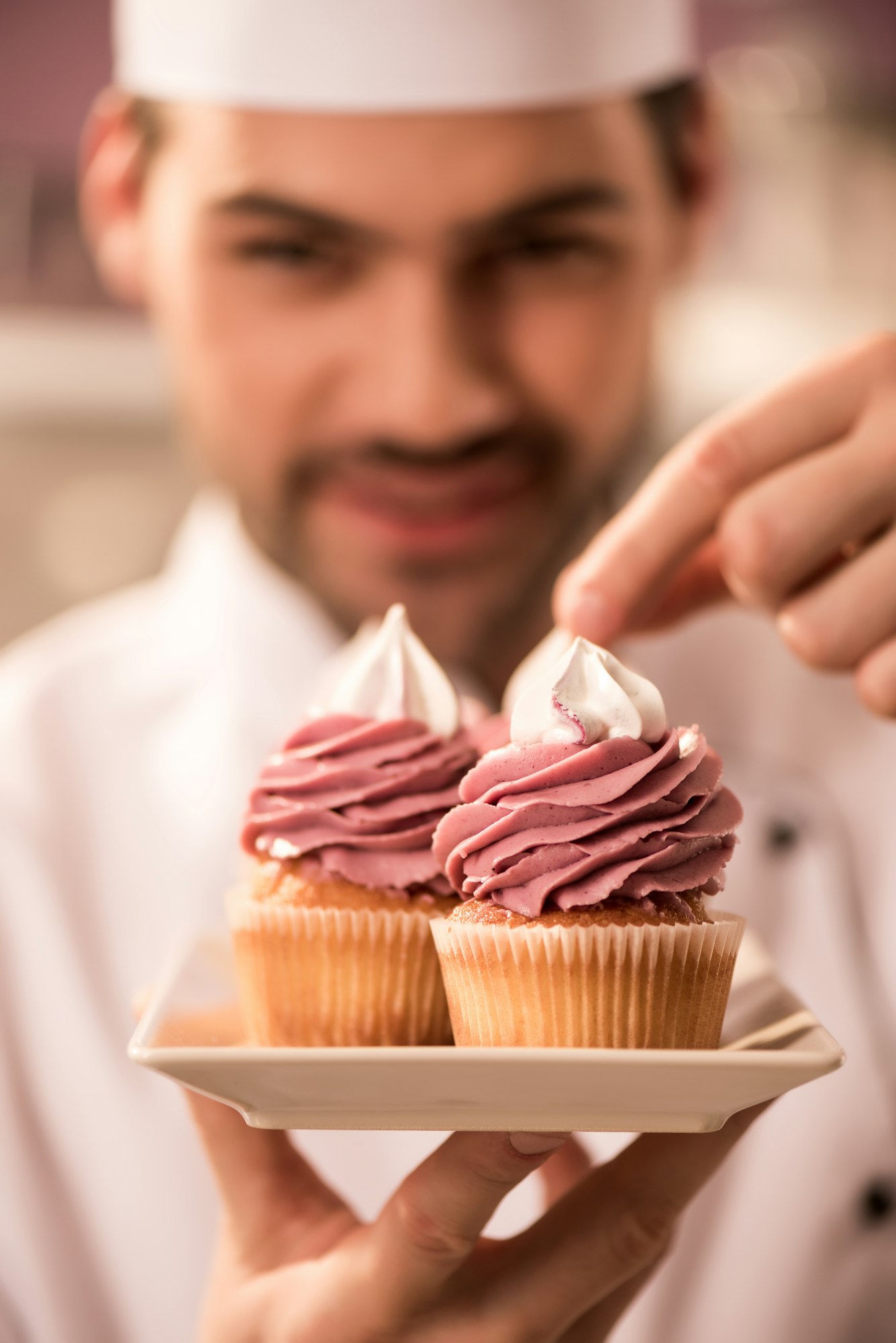 selective focus of confectioner decorating cupcakes in restaurant kitchen